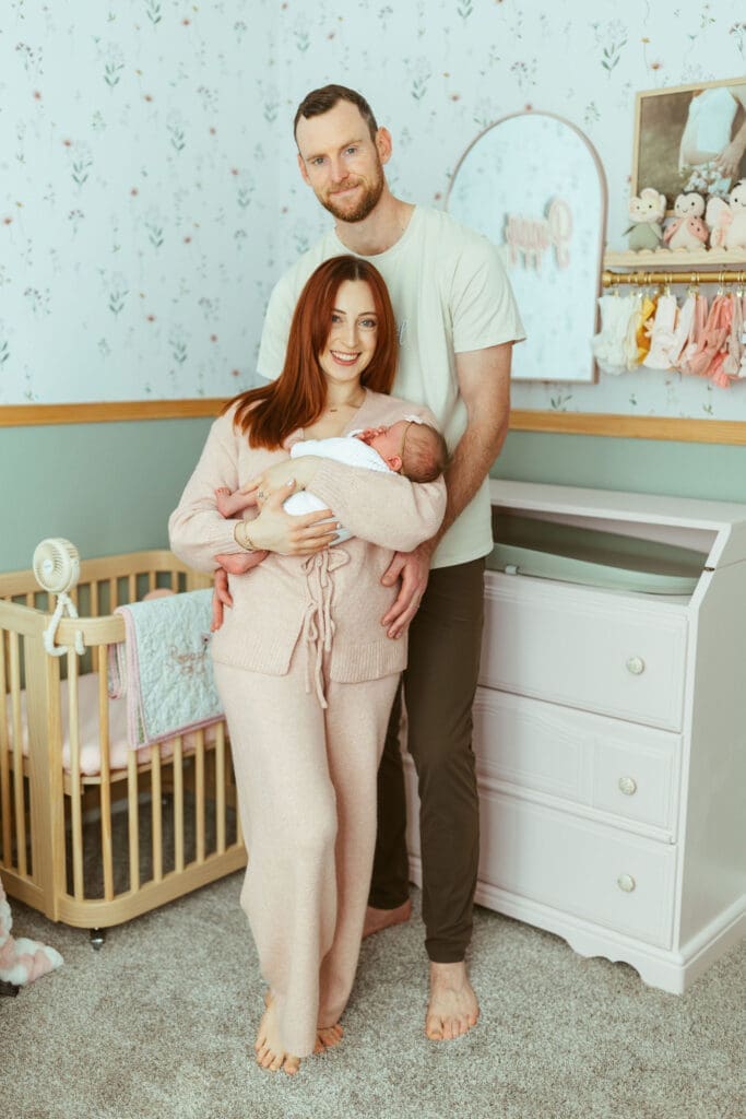 Arizona newborn photographer documenting newborn baby girl sleeping peacefully beside floral wallpaper and pastel nursery decor