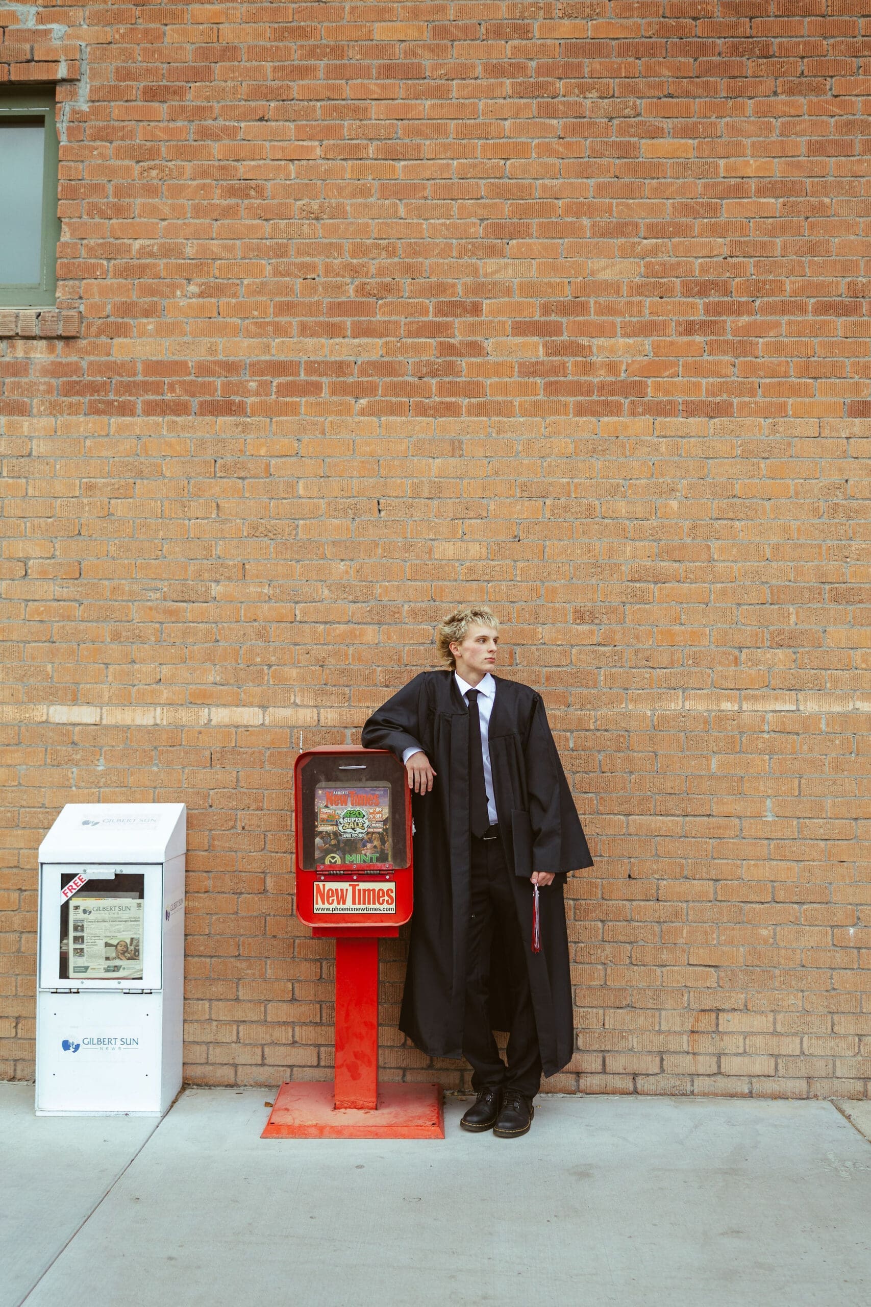 Phoenix senior photographer capturing high school senior standing beside vintage newspaper box in downtown urban setting during Arizona senior portrait session