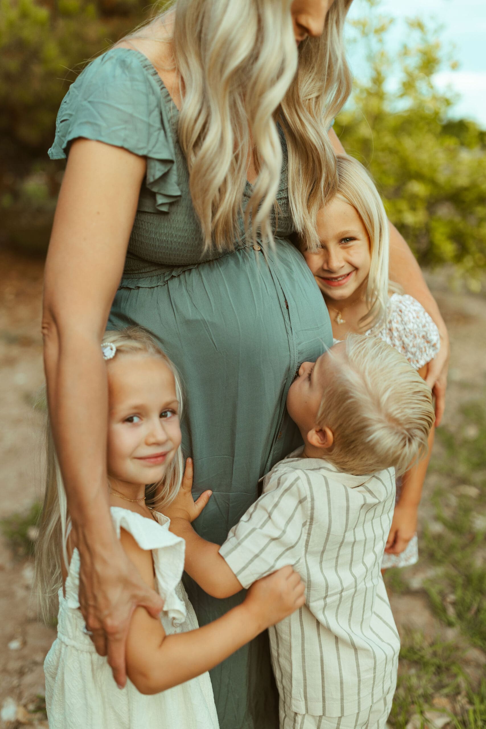 Phoenix maternity photographer capturing three excited siblings hugging their mother's baby bump during family maternity session at Hagen Farms in Queen Creek Arizona