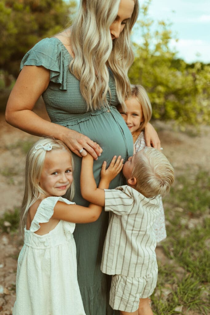 Family maternity photography featuring siblings cuddling pregnant mother during outdoor maternity session near Phoenix Arizona