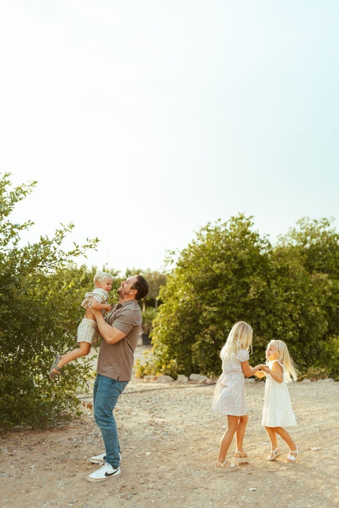 Father lifting son during family maternity photography session at Hagen Farms in Queen Creek Arizona