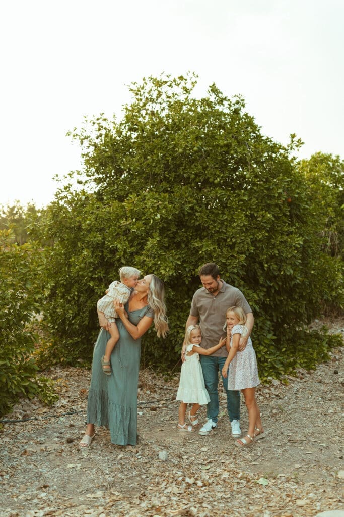 Expecting mother cuddling son while family gathers during outdoor maternity session in Queen Creek Arizona