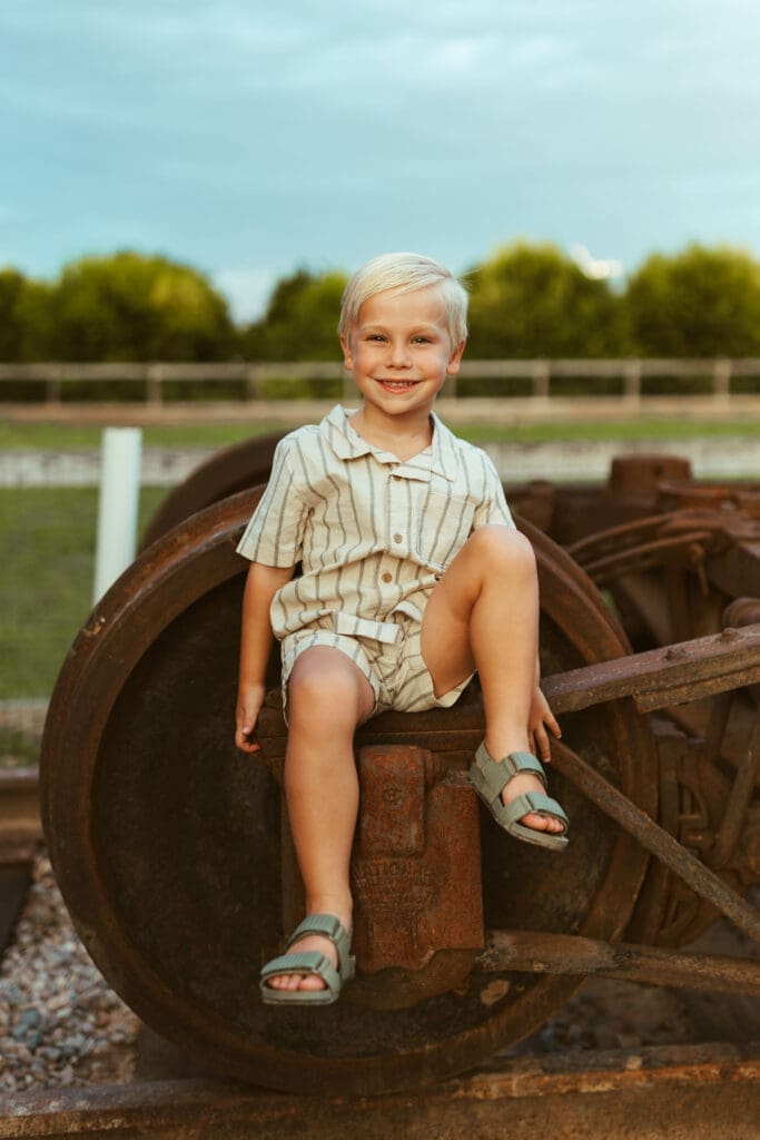 Young boy sitting on vintage farm equipment during family maternity photography session in Queen Creek Arizona