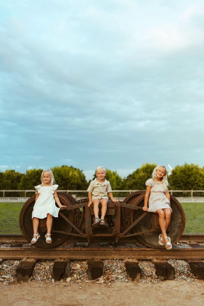 Three siblings sitting on vintage farm equipment during family maternity photography session in Queen Creek Arizona