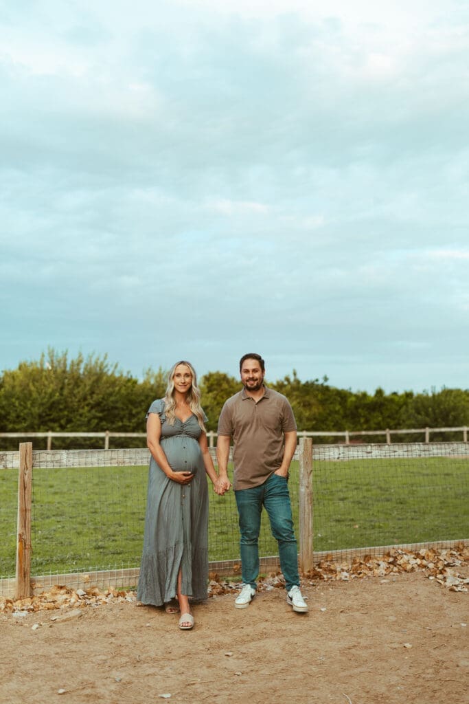 Phoenix maternity photographer capturing expecting parents holding hands during maternity session at Hagen Farms in Queen Creek Arizona