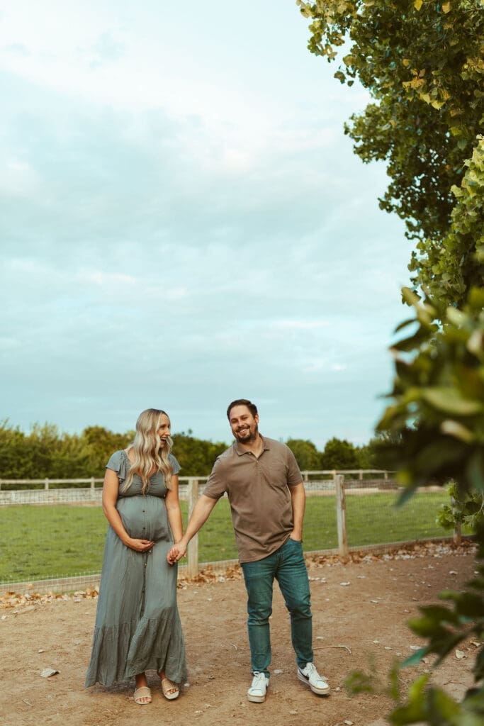 Expecting parents walking hand in hand during outdoor maternity photography session at Hagen Farms near Phoenix Arizona