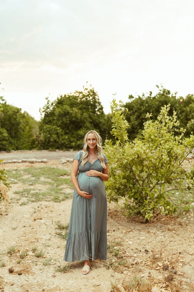 Pregnant mother posing beside citrus trees during outdoor maternity session at Hagen Farms in Queen Creek Arizona