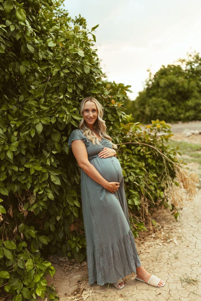 Pregnant mother posing beside citrus trees during outdoor maternity session at Hagen Farms in Queen Creek Arizona