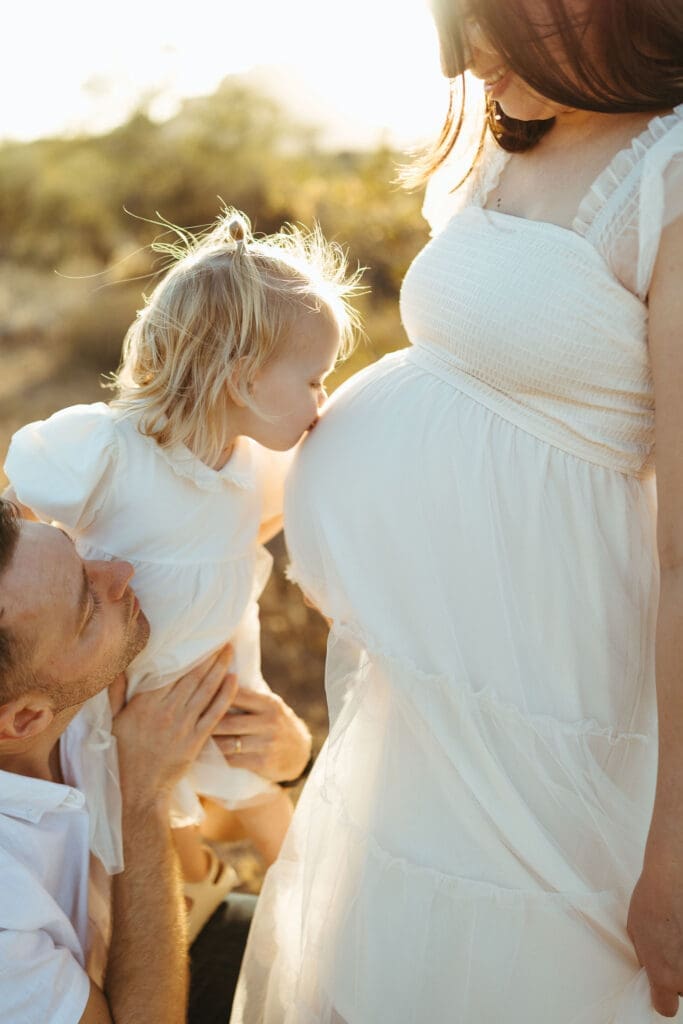 Scottsdale maternity photographer capturing toddler kissing mother's baby bump during luxury Arizona desert maternity session