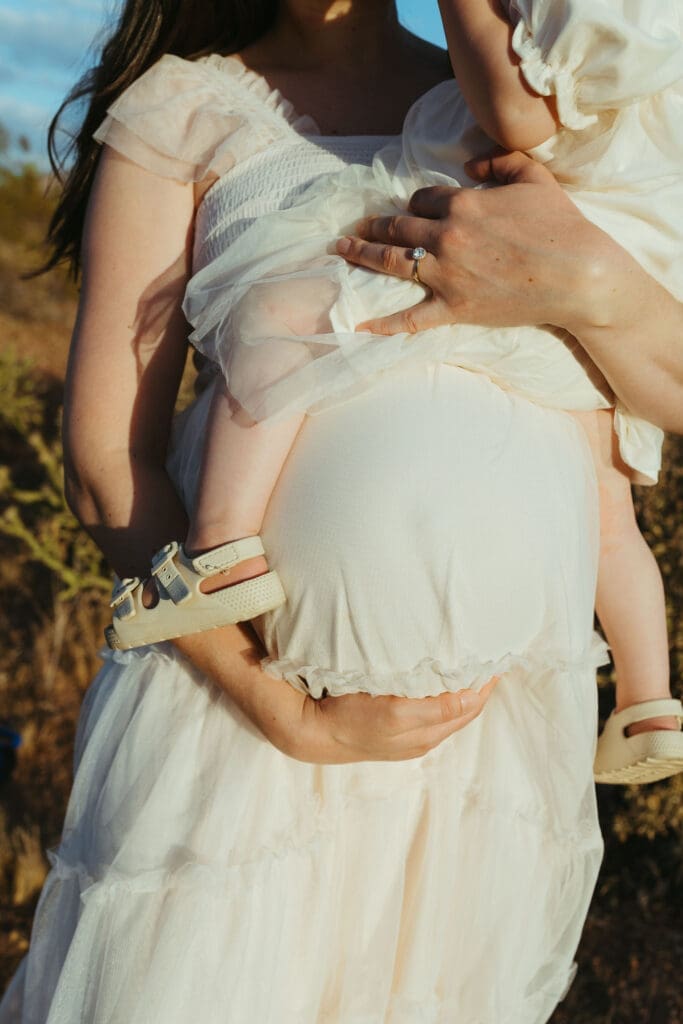 Arizona maternity photography featuring close-up of baby bump and toddler cuddling expecting mother during outdoor maternity session