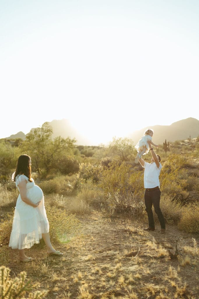 Mesa maternity photographer capturing father lifting toddler into the air during golden hour desert maternity session at Phon D Sutton Recreation Area