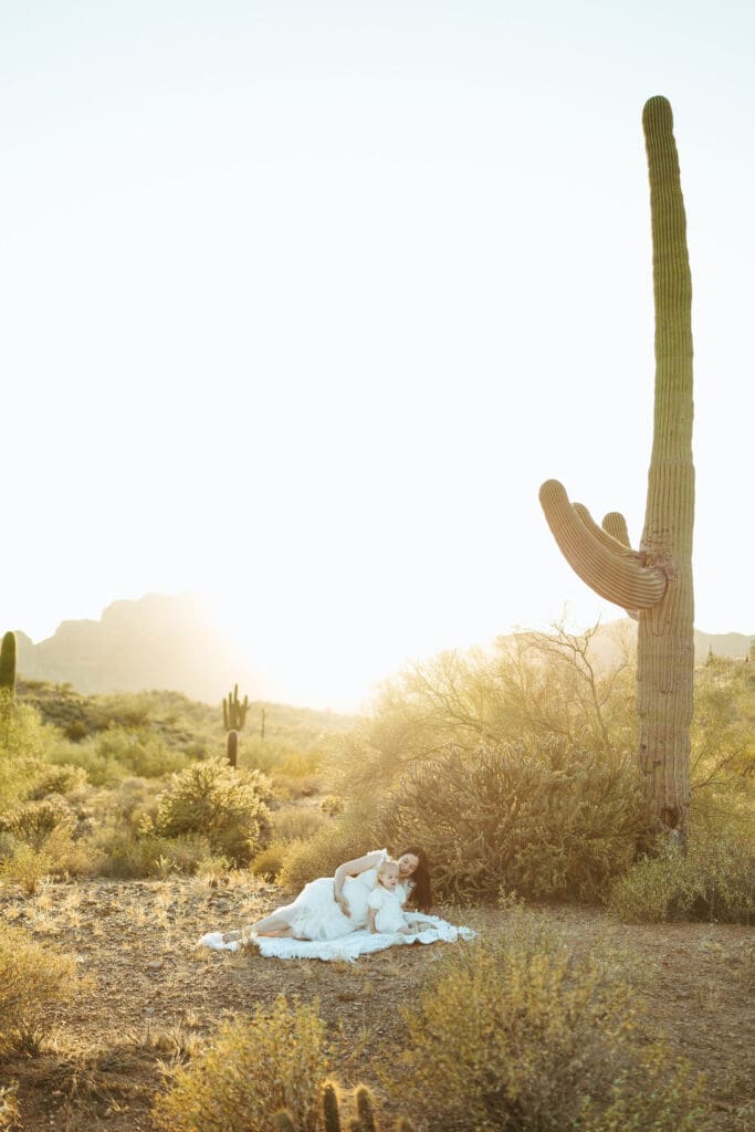 Scottsdale maternity photographer capturing expecting mother and toddler relaxing on blanket during sunset desert maternity session