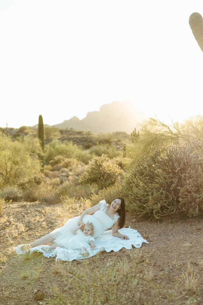 Scottsdale maternity photographer capturing expecting mother and toddler relaxing on blanket during sunset desert maternity session