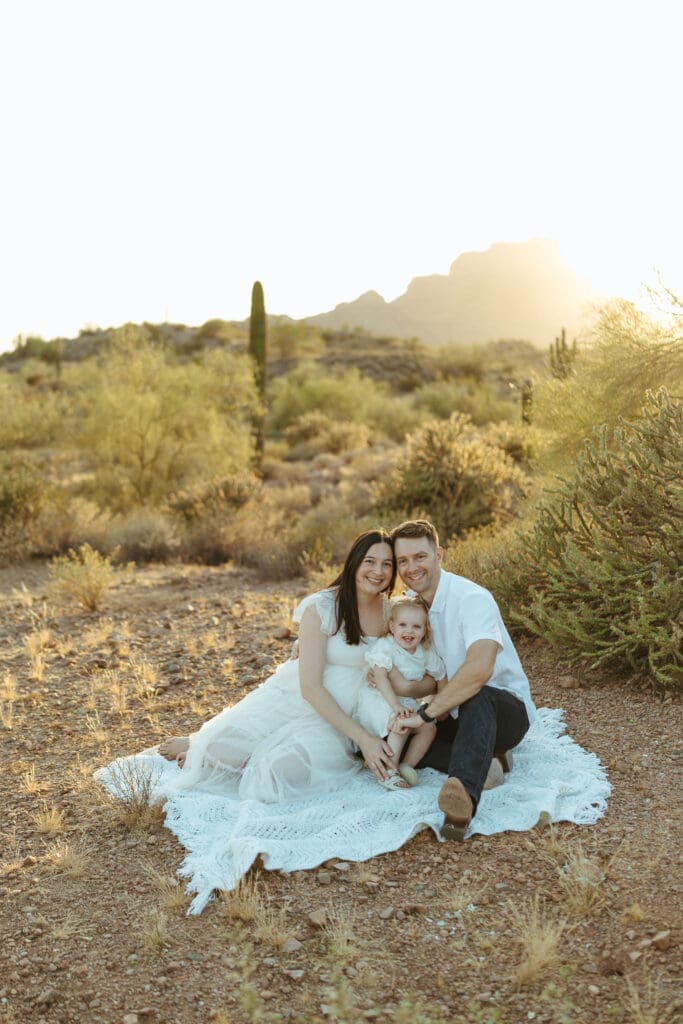 Scottsdale maternity photographer capturing family of three cuddling together during sunset maternity session in Arizona desert