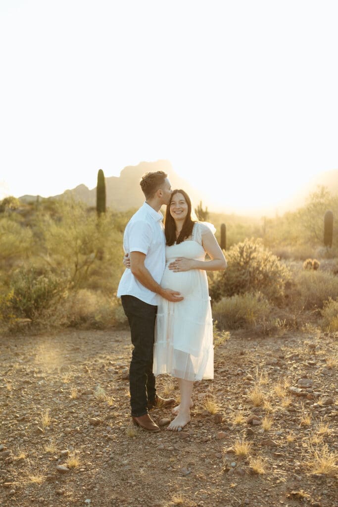 Mesa maternity photographer capturing expecting parents embracing during golden hour desert maternity session at Phon D Sutton Recreation Area in Arizona
