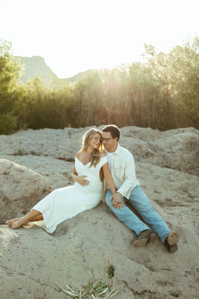 Pregnant couple walking hand in hand along the Salt River during a golden hour maternity session in Mesa Arizona.