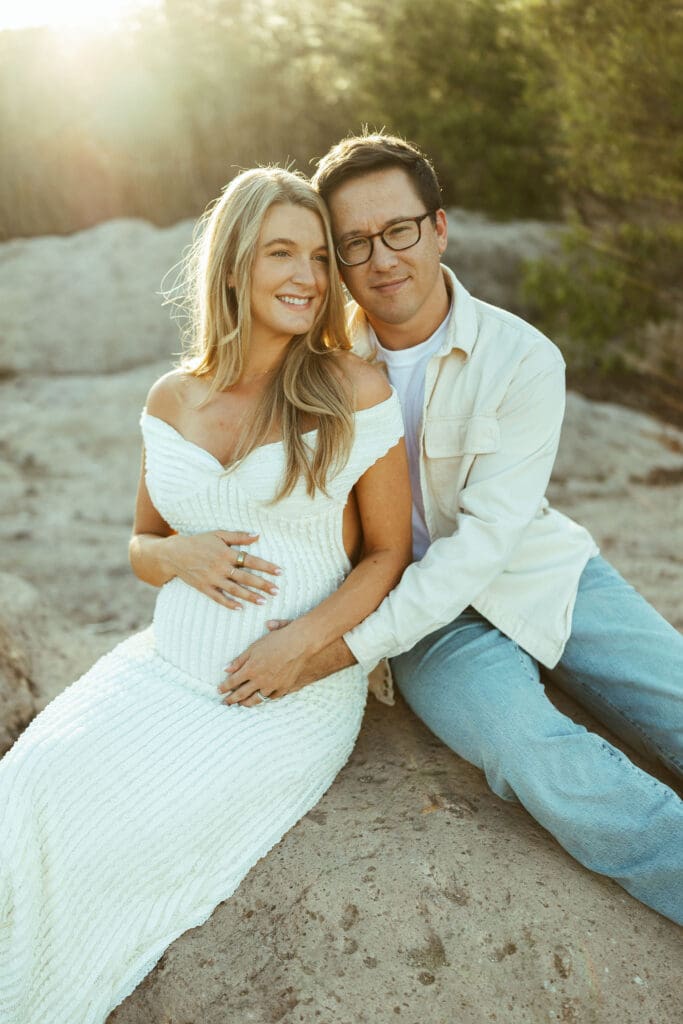 Mother-to-be standing barefoot in the Salt River wearing a fitted white maternity dress during sunset in Mesa Arizona.