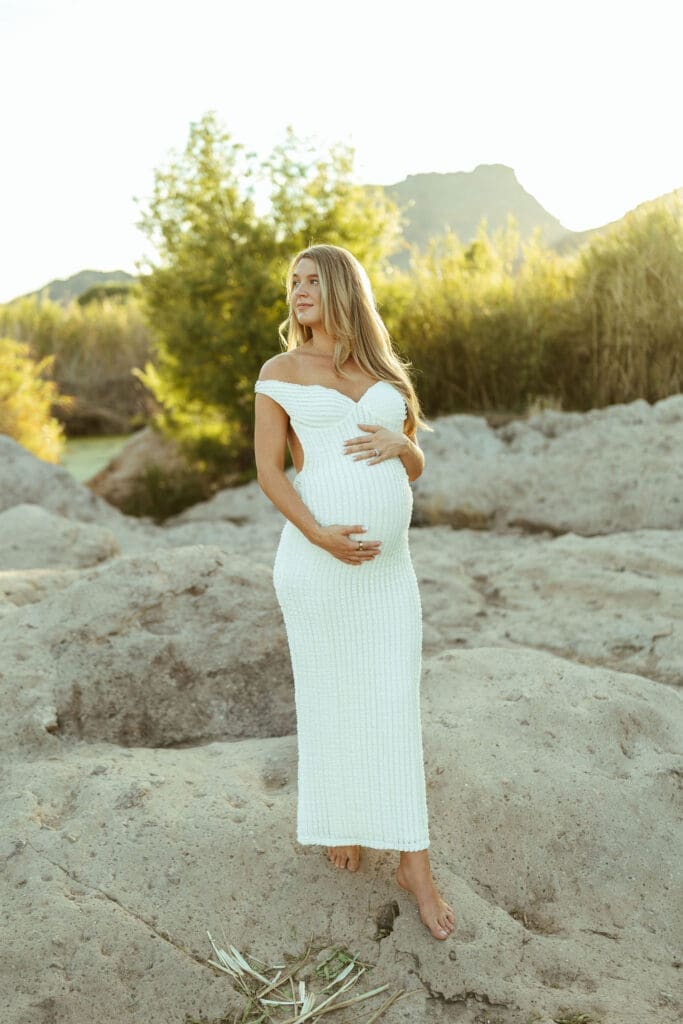 Pregnant woman posing on river rocks during a sunset maternity session at the Salt River in Mesa Arizona.