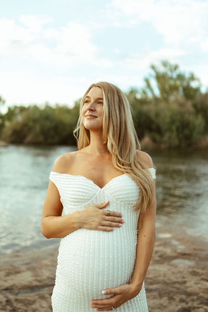 Outdoor maternity portrait of expecting mother standing beside the Salt River with glowing golden hour light in Mesa Arizona.