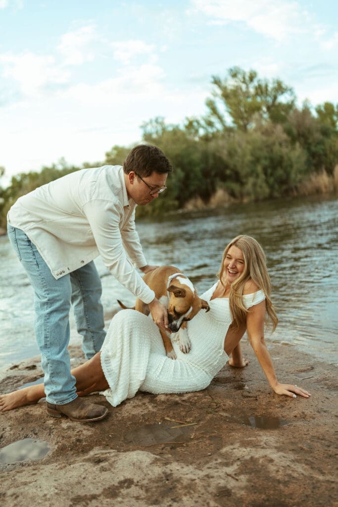 Couple laughing while holding their dog during a candid maternity session at Phon D Sutton Recreation Area in Mesa Arizona.