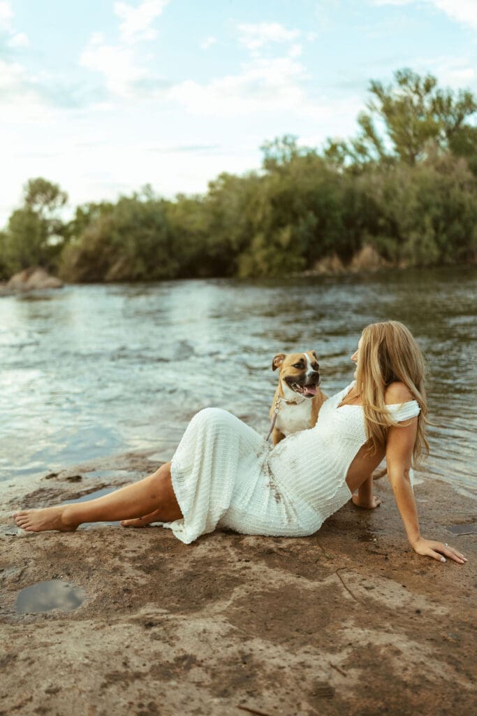 Maternity session with family dog at Phon D Sutton Recreation Area featuring a pregnant mother relaxing beside the river in Arizona.