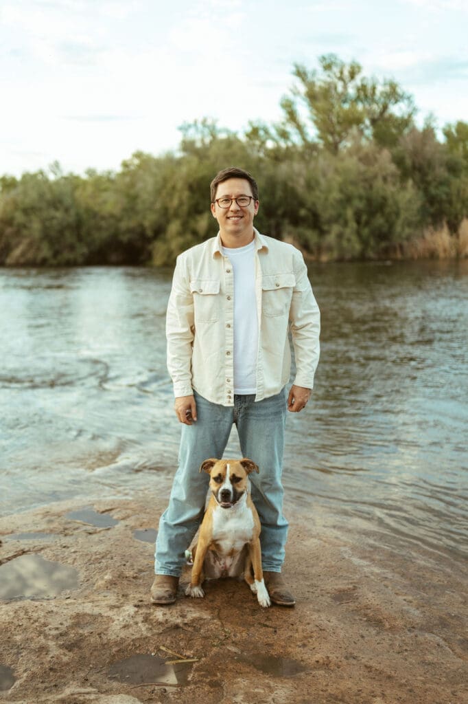 Father-to-be standing beside the Salt River with family dog during a maternity session in Mesa Arizona.