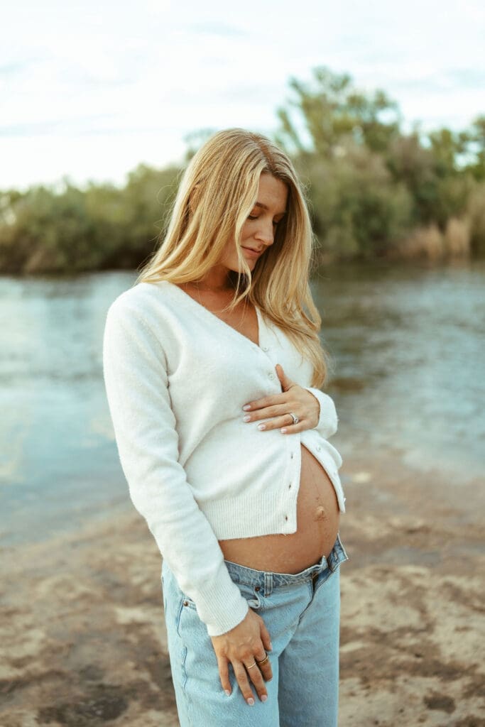 Close-up maternity portrait of expecting mother holding her baby bump beside the Salt River at golden hour.