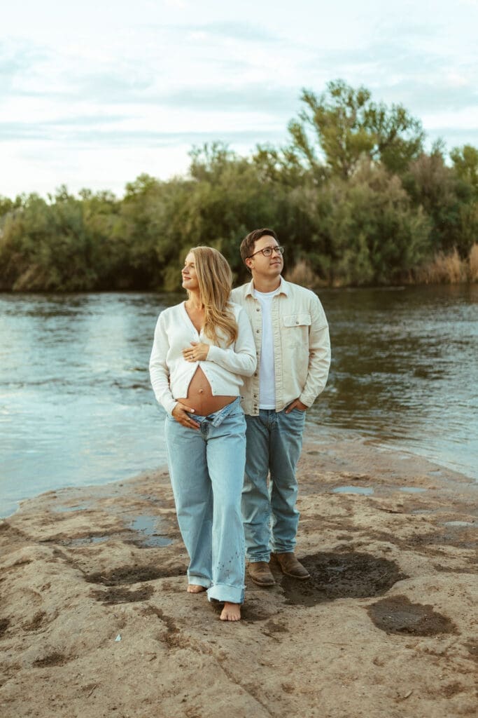 Expecting couple walking together beside the Salt River during a romantic maternity session at sunset.