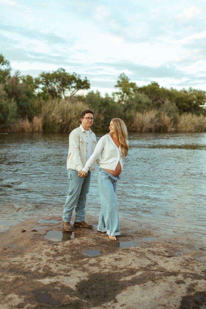 Romantic maternity portraits with barefoot walking and soft sunset light beside the Salt River.