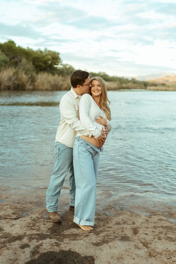 Outdoor maternity portrait of expecting parents embracing beside the Salt River in Mesa Arizona.