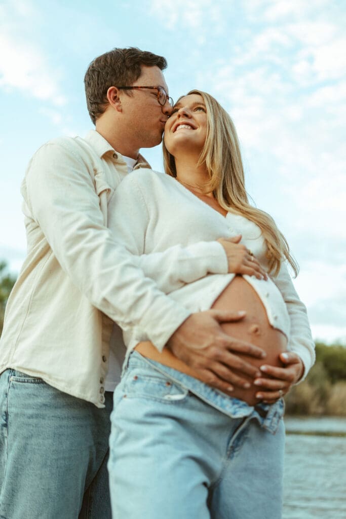 Outdoor maternity photo of pregnant mom and dad smiling beside the Salt River during sunset in Mesa Arizona.