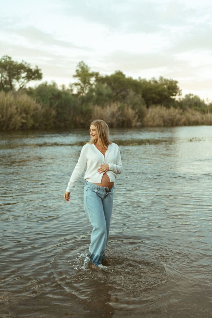 Pregnant woman smiling while standing in the river during a romantic Arizona maternity session.