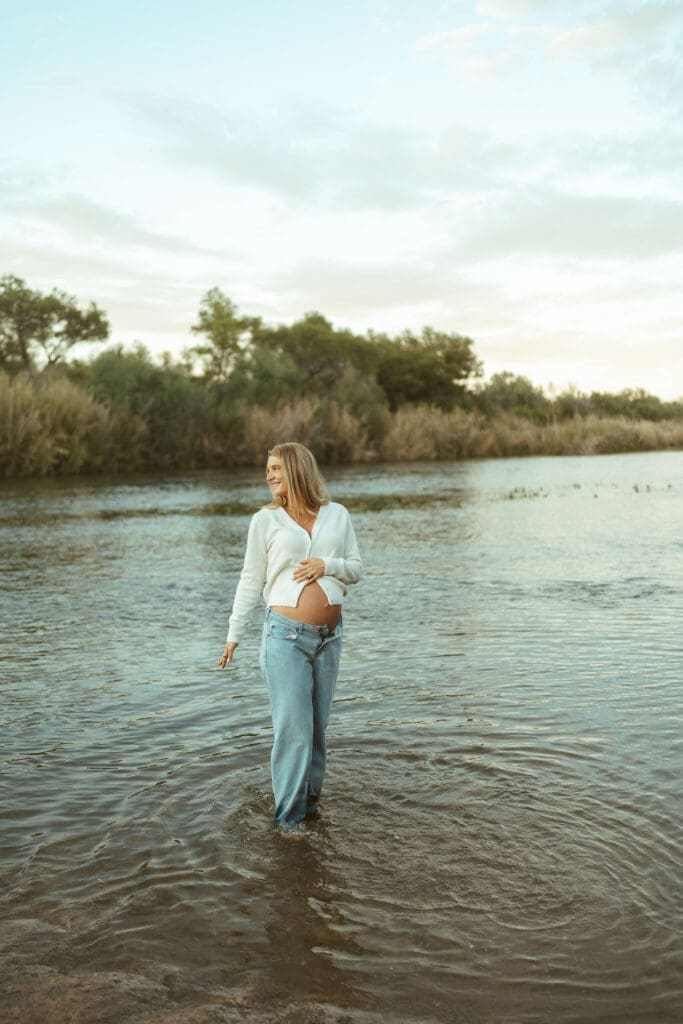 Expecting mother posing in flowing river water during a golden hour maternity session in Arizona.
