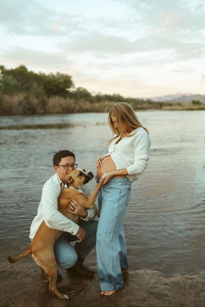 Father-to-be kneeling beside family dog during a maternity session at Phon D Sutton Recreation Area.