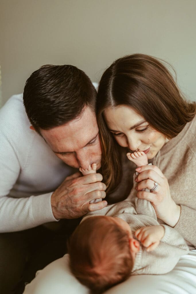 Lifestyle newborn photographer in Scottsdale AZ capturing emotional newborn family portraits with neutral styling and natural light photography, kissing baby toes