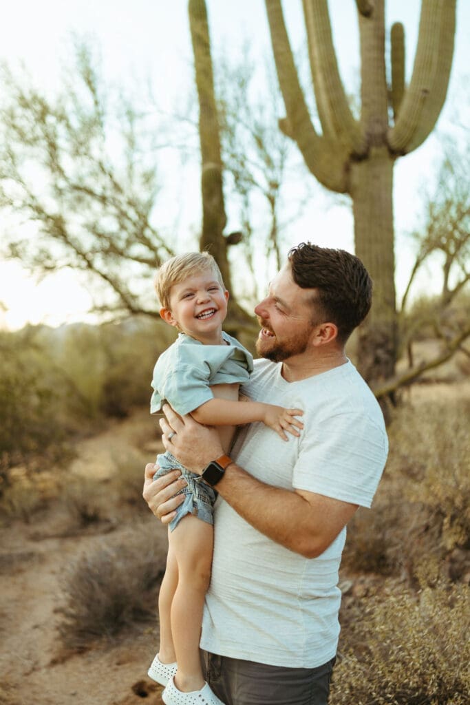Father lifting toddler son during golden hour family photography session near Lost Dutchman State Park Arizona