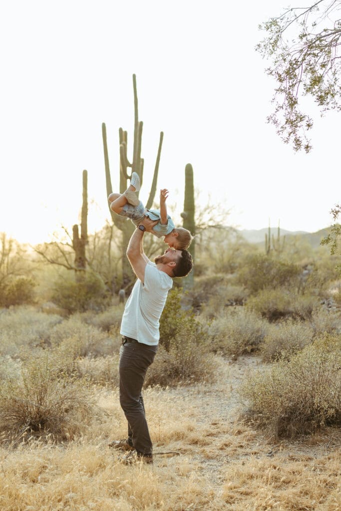 Candid family photography session in Phoenix Arizona with toddler being lifted into the air at sunset