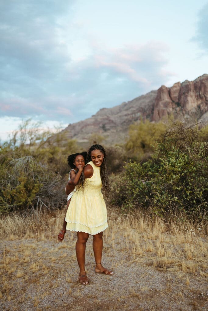 Mother giving her daughter a piggyback ride during a family session with the Superstition Mountains in the background