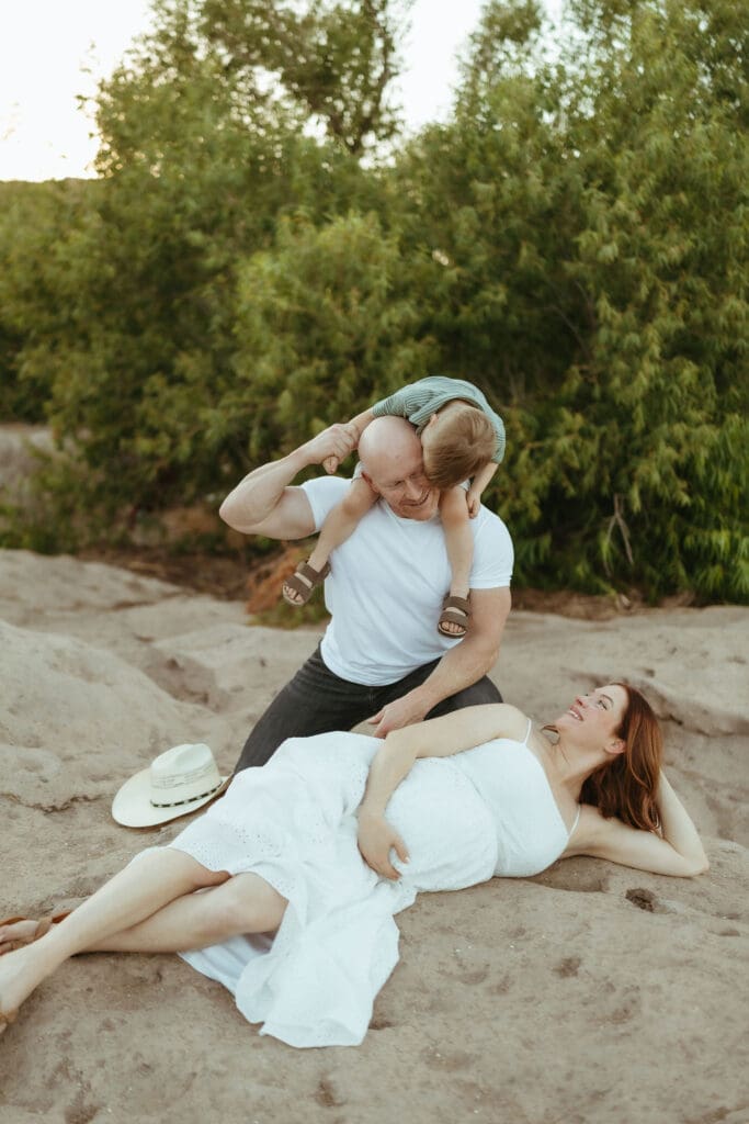 Expecting mother laughing with her husband and toddler during an outdoor maternity session in Mesa, Arizona.