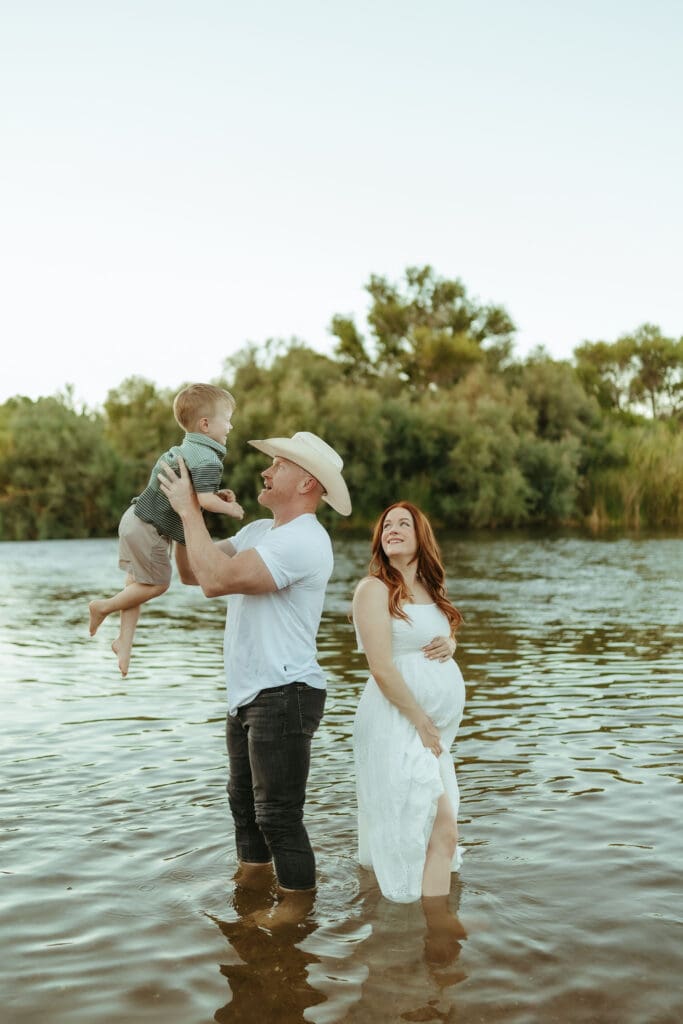 Father lifting his toddler above the Salt River during an outdoor family maternity session in Mesa, Arizona.