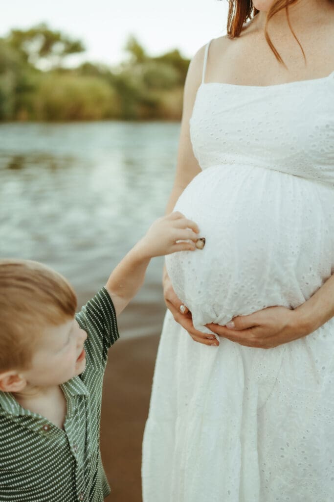 Toddler gently touching his mother's pregnant belly during a family maternity session in Mesa, Arizona.