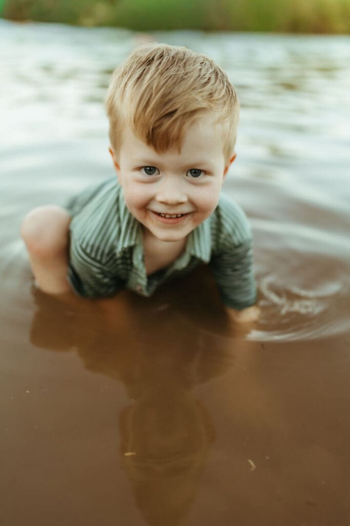 Smiling toddler playing in the shallow water during an outdoor family maternity session at the Salt River.