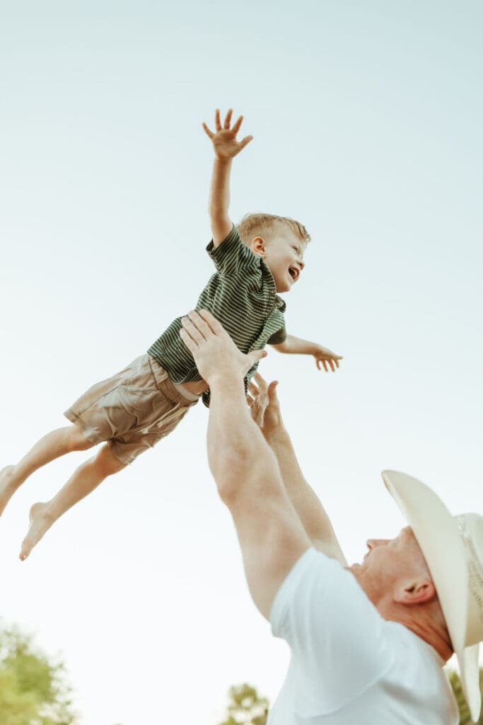 Father lifting his toddler into the air during a joyful maternity session at the Salt River in Mesa, Arizona.