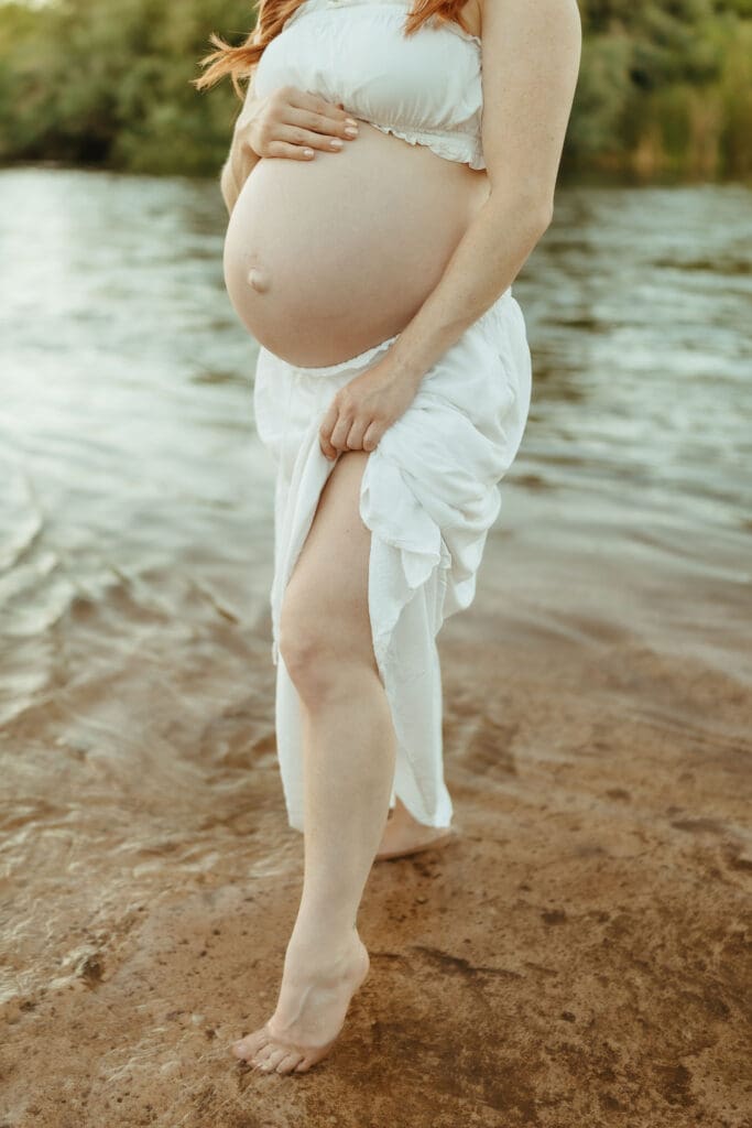 Close-up maternity photo of a pregnant belly beside the Salt River during an outdoor maternity session.