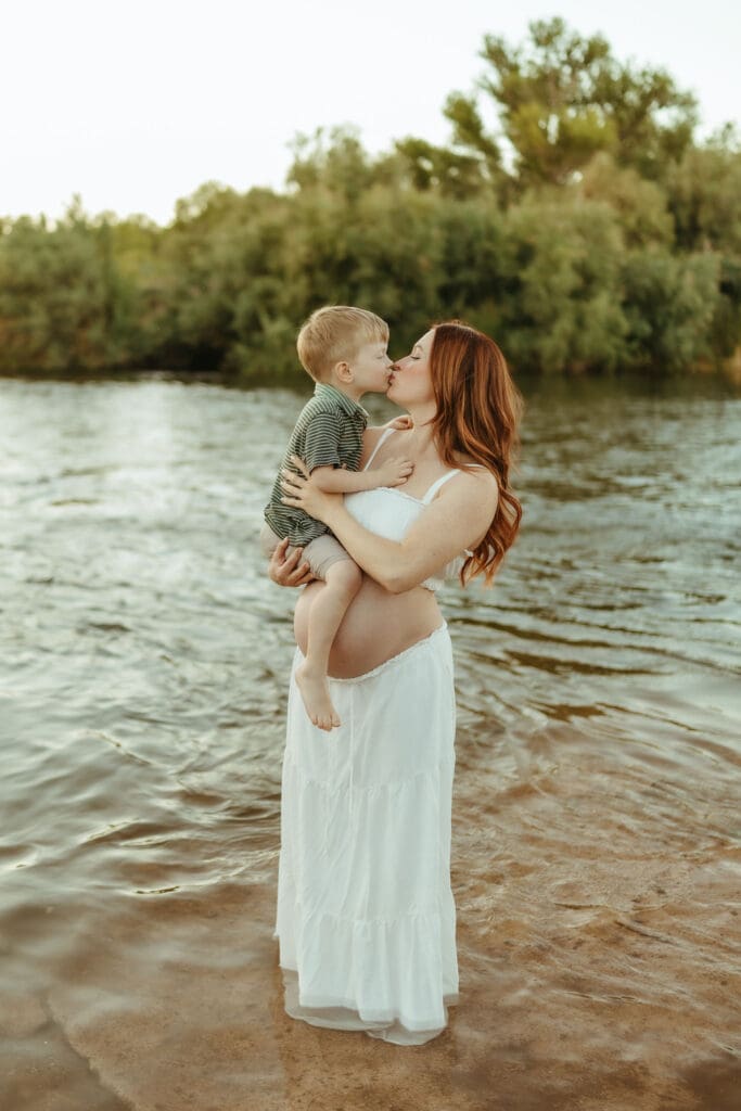 Pregnant mother kissing her toddler during a Salt River maternity session at Phon D Sutton Recreation Area in Mesa, Arizona.