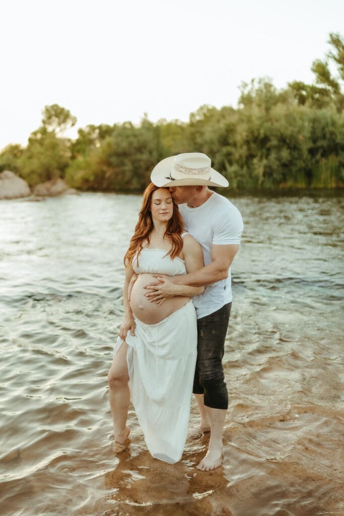 Expecting parents embracing in the Lower Salt River during golden hour maternity photos in Mesa, Arizona.