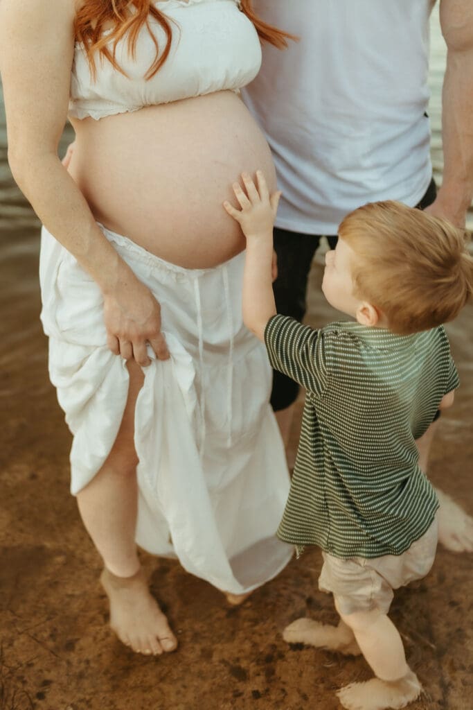 Toddler touching his mother's pregnant belly during a family maternity session at the Salt River in Arizona.