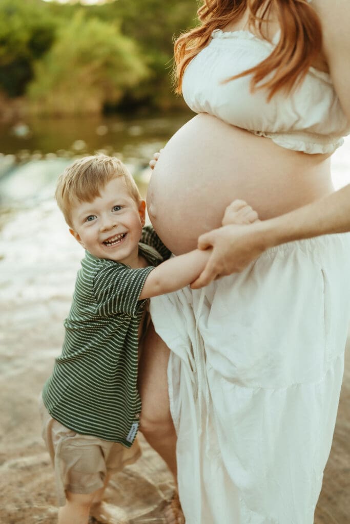 Smiling toddler hugging his mother's baby bump during a Mesa maternity photography session.