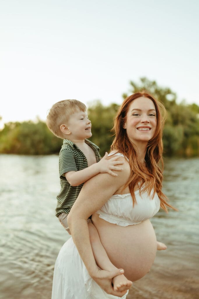 Pregnant mother carrying her toddler during an outdoor maternity photography session in Mesa, Arizona.