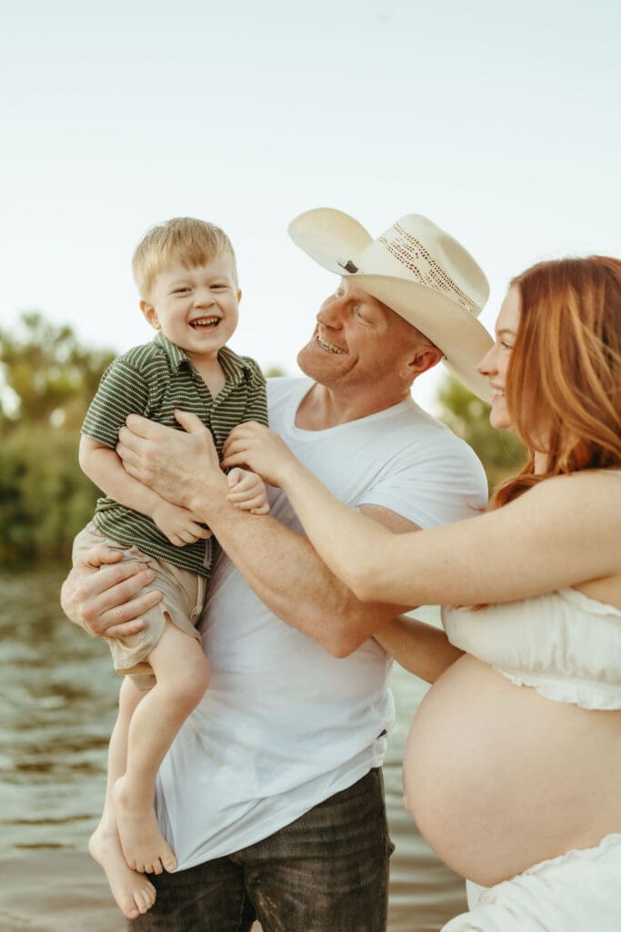 Father holding his smiling toddler during a family maternity session at the Salt River in Mesa, Arizona.